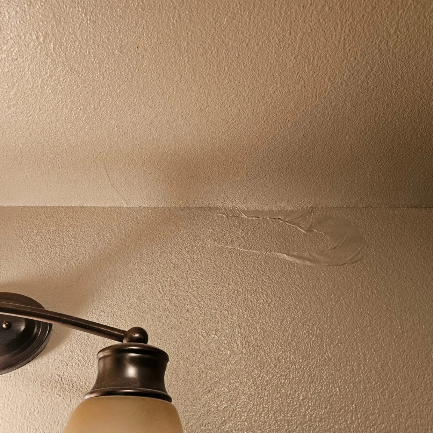 Cracked drywall patch above bronze vanity light